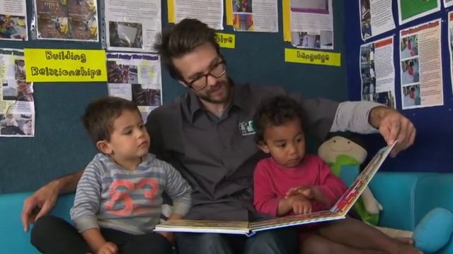 Man reading story to two young boys in classroom.