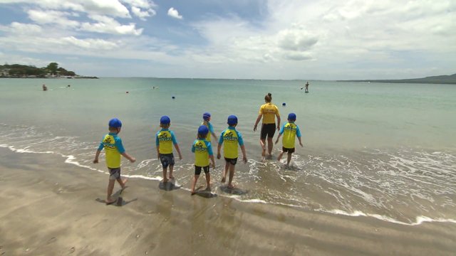 Kids learning surf life saving skills with teacher at beach.