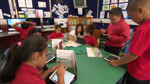 Children in classroom seated around table with ipads.