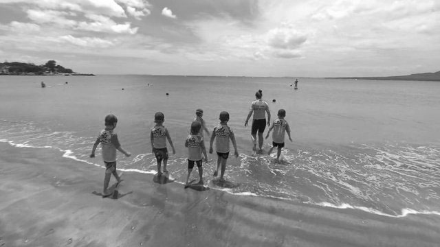 Kids learning surf life saving skills with teacher at beach.