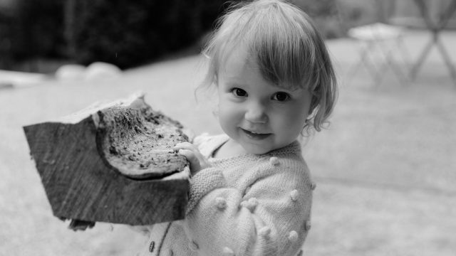 Child carries piece of wood outside with smile.