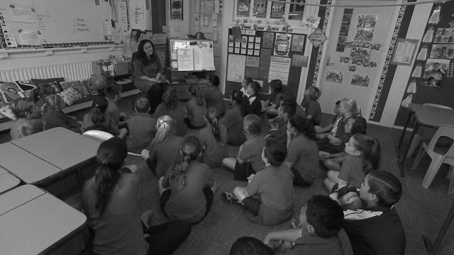 Children all seated in classroom listening to teacher.