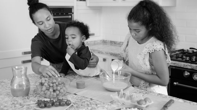 Mother with two children prepares food in the kitchen together.